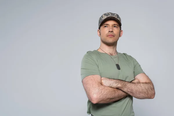Military man in t-shirt and cap standing with folded arms during memorial day isolated on grey — Stock Photo