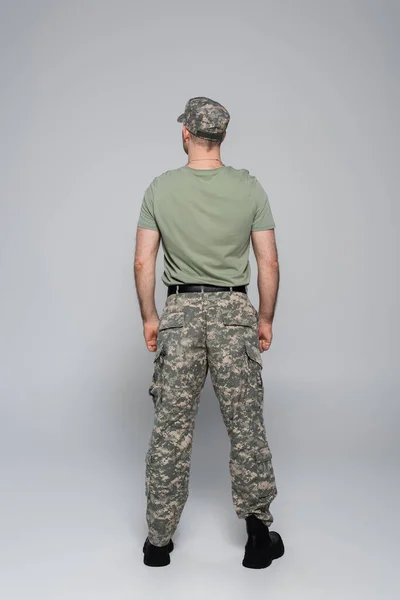 Back view of serviceman in military uniform and cap standing on grey — Stock Photo