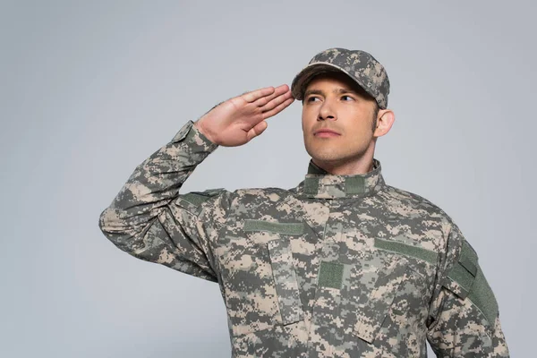 Patriota americano em uniforme militar com boné saudando durante o dia comemorativo isolado em cinza — Fotografia de Stock