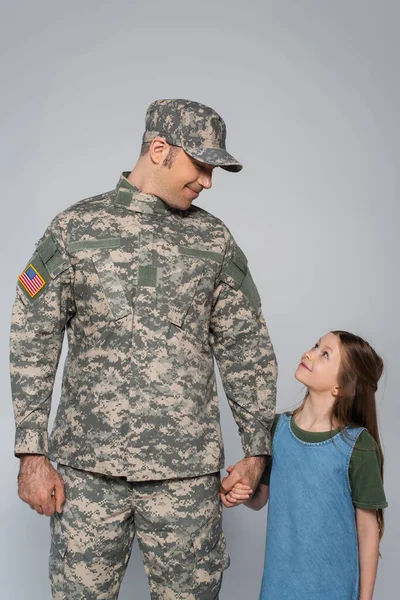 Glücklicher Soldat in Militäruniform Händchen haltend mit fröhlicher Tochter am Gedenktag isoliert auf grau — Stockfoto