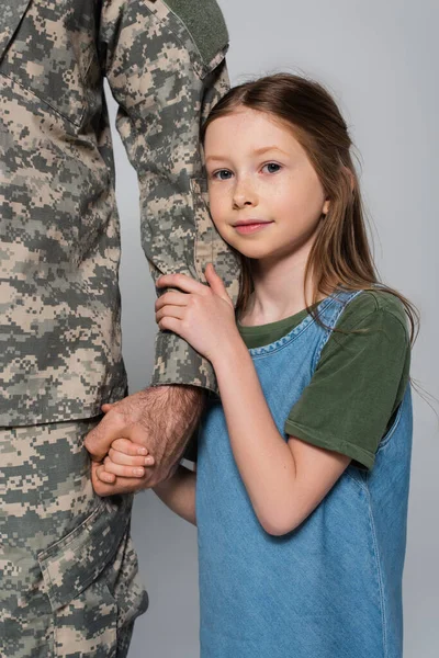 Linda niña preadolescente abrazando la mano del padre en uniforme militar aislado en gris - foto de stock