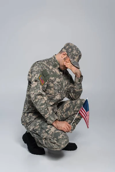 Army soldier crying and covering face while holding flag of United States during memorial day on grey — Stock Photo