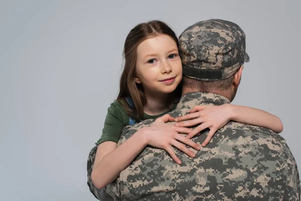 Preteen kid hugging serviceman in military uniform and cap during memorial day isolated on grey — Stock Photo