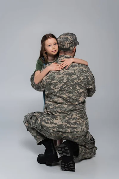 Preteen kid hugging serviceman in military uniform during memorial day on grey — Stock Photo