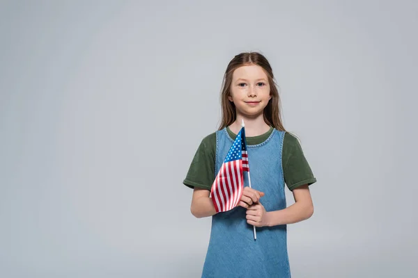 Patriótico preteen menina sorrindo enquanto segurando bandeira da América durante memorial dia isolado no cinza — Fotografia de Stock