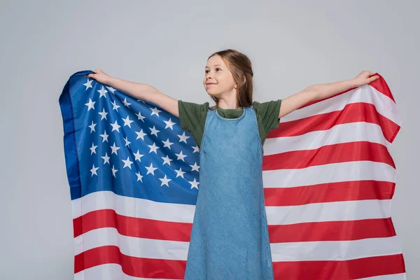 Patriotic preteen girl smiling while holding huge flag of America during memorial day isolated on grey — Stock Photo