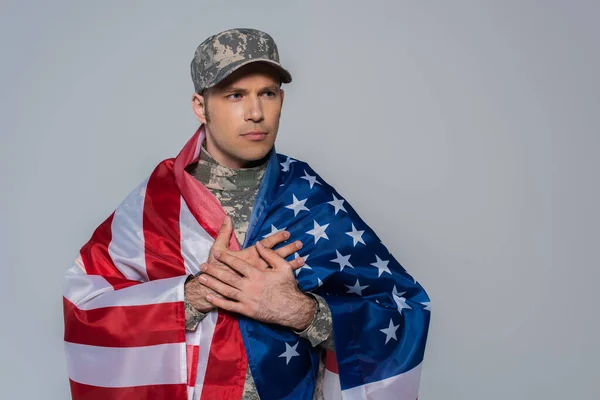 Patriotic soldier in camouflage uniform wrapped in flag of United States of America during memorial day isolated on grey — Stock Photo