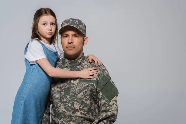 Preteen girl hugging father in army uniform during memorial day isolated on grey — Stock Photo