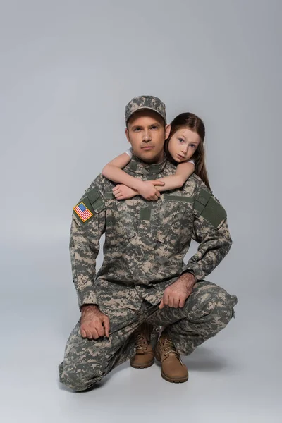 Preteen kid hugging brave father in army uniform during memorial day on grey — Stock Photo