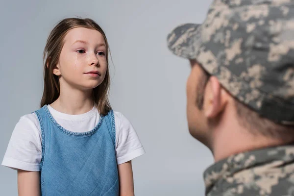 Девочка-подросток смотрит на храброго отца в военной форме на размытом переднем плане, изолированном на сером — стоковое фото