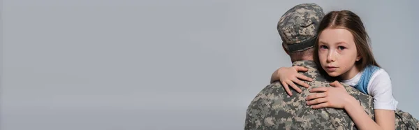Patriotisches Mädchen umarmt Vater in Armeeuniform und weint am Gedenktag isoliert auf grauem Banner — Stockfoto