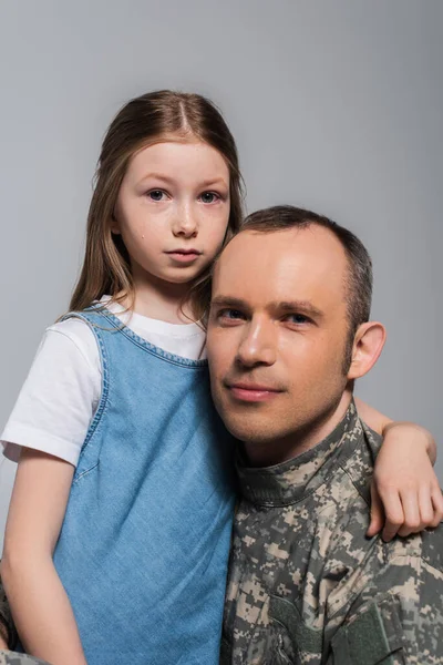 Niño patriótico abrazando al soldado en uniforme del ejército y llorando durante el día conmemorativo aislado en gris - foto de stock