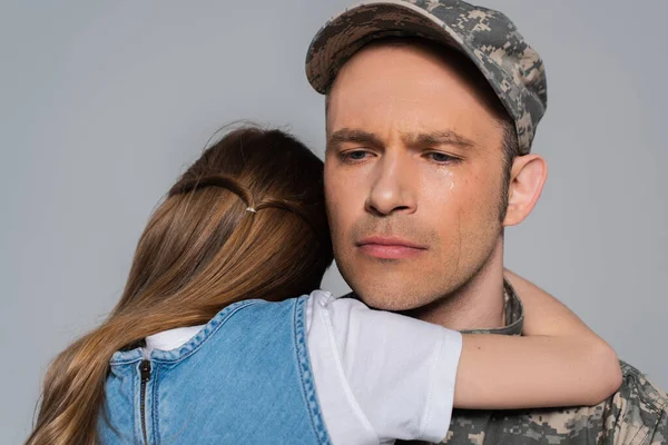 Грустный военнослужащий в военной форме плачет и обнимается с дочерью во время памятного дня, изолированного на сером — стоковое фото