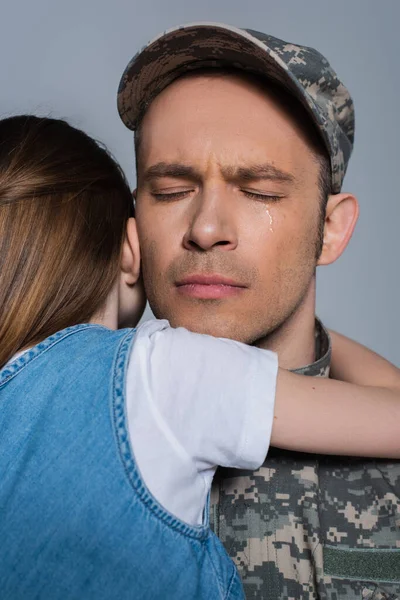 Сентиментальный военнослужащий в военной форме плачет и обнимается с дочерью в день памяти, изолированный от серых — стоковое фото