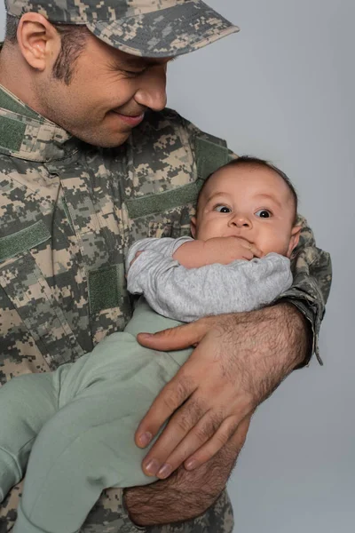 Happy soldier in military uniform and cap holding newborn son isolated on grey — Stock Photo