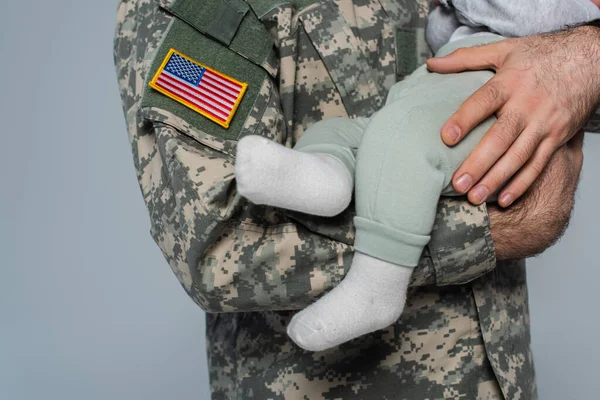 Vue recadrée d'un soldat américain en uniforme tenant un nouveau-né isolé sur du gris — Photo de stock