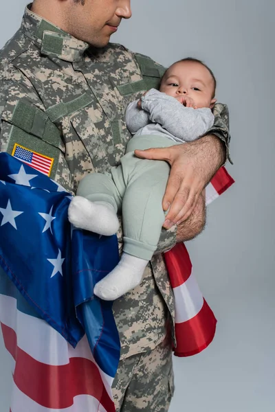 Patriotischer Soldat in Uniform steht mit der Flagge Amerikas und hält einen kleinen Jungen in den Armen auf grau — Stockfoto