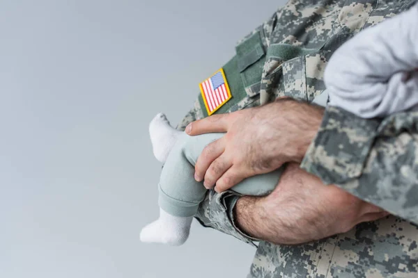 Vista recortada del soldado americano en uniforme que sostiene al bebé recién nacido aislado en gris - foto de stock