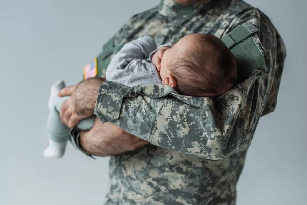 Ausgeschnittene Ansicht eines Soldaten in Uniform, der Neugeborenes isoliert auf grau hält — Stockfoto