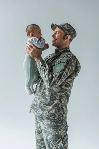 Soldado militar feliz em uniforme segurando filho recém-nascido em armas isoladas em cinza — Fotografia de Stock