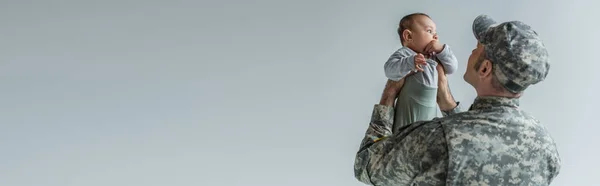 Soldato dell'esercito in uniforme e berretto con bambino in braccio isolato su grigio, stendardo — Foto stock