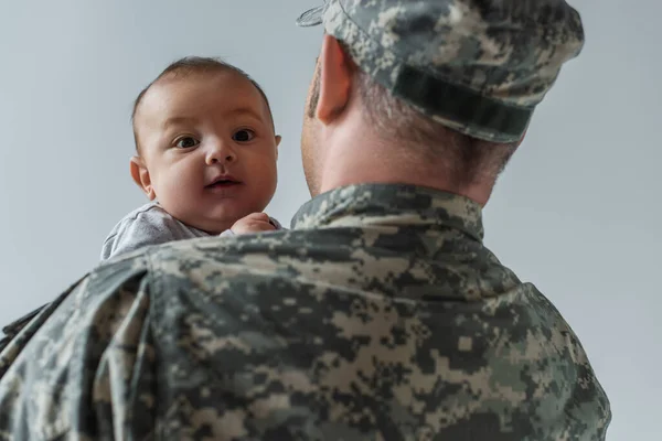 Neugeborener Junge in den Armen eines Soldaten in Militäruniform isoliert auf grau — Stockfoto