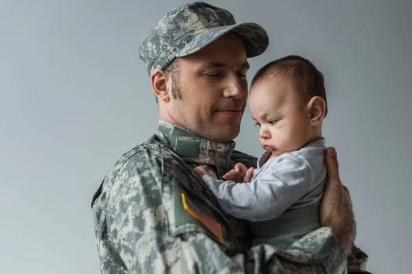American serviceman in military uniform holding in arms newborn son isolated on grey — Stock Photo