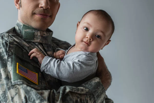 Американский военнослужащий в форме, держащий в руках новорожденного мальчика, изолированного на сером — стоковое фото