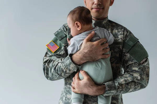 Soldado americano de uniforme segurando em armas menino recém-nascido isolado em cinza — Fotografia de Stock