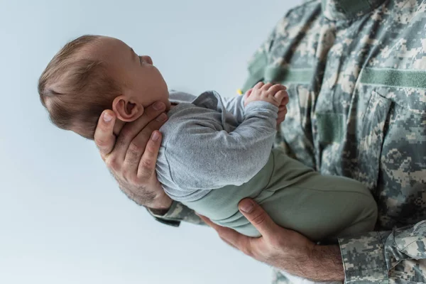 Soldat en uniforme tenant dans les bras le fils nouveau-né isolé sur gris — Photo de stock