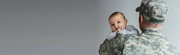 Serviceman in military uniform and cap hugging newborn son isolated on grey, banner — Stock Photo