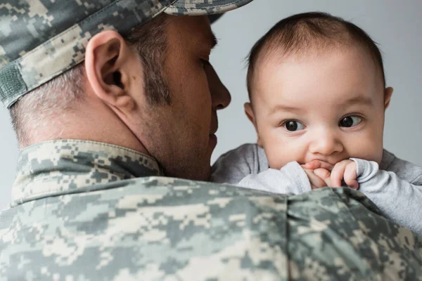Man in military uniform and cap hugging newborn son isolated on grey — Stock Photo