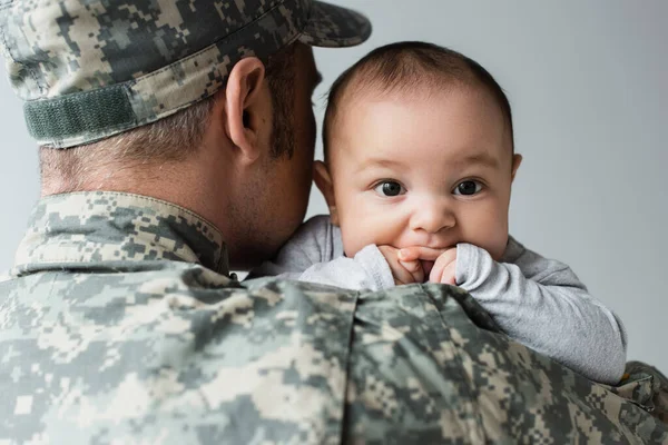 Man in army uniform and cap hugging newborn son isolated on grey — Stock Photo