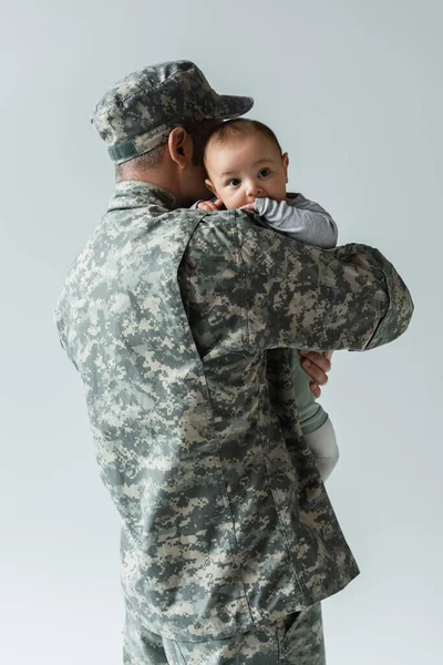 Man in army uniform and military cap hugging newborn son isolated on grey — Stock Photo