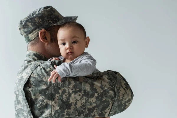Батько у військовій формі та малюк, що обіймає немовля, відокремлений від сірого — стокове фото