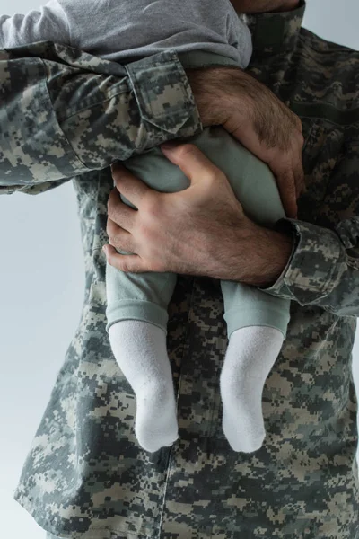 Vista recortada del padre en uniforme militar abrazando hijo bebé aislado en gris - foto de stock