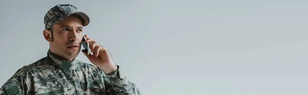Serviceman in cap and army uniform having conversation on smartphone isolated on grey, banner — Stock Photo