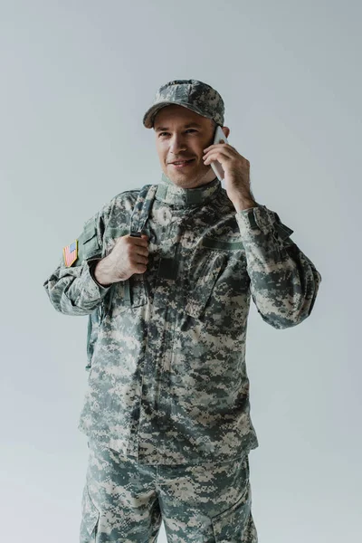 Happy serviceman in army uniform talking on smartphone isolated on grey — Stock Photo