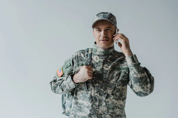 Alegre militar en uniforme del ejército hablando en teléfono inteligente aislado en gris - foto de stock