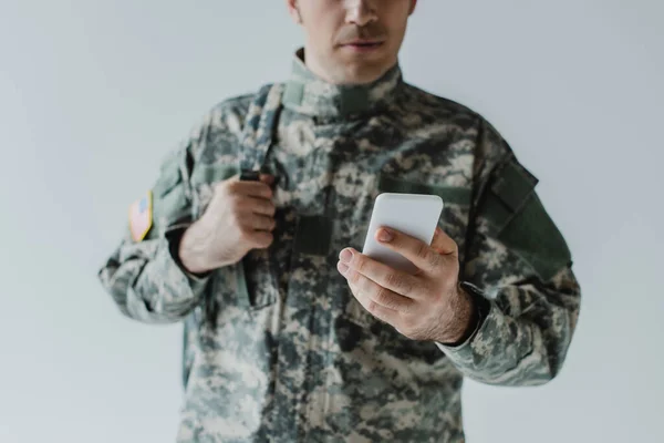 Vista recortada del militar en uniforme del ejército utilizando el teléfono móvil aislado en gris - foto de stock
