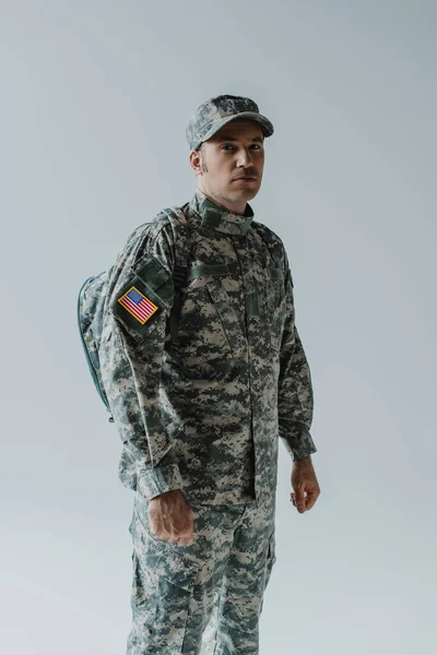 Soldado americano en uniforme del ejército con bandera nacional de pie aislado en gris - foto de stock