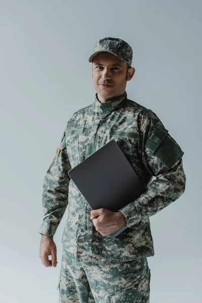 Beau soldat en uniforme de l'armée et casquette debout avec ordinateur portable isolé sur gris — Photo de stock