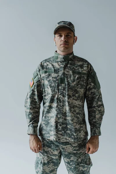 Soldat en uniforme militaire et écouteurs sans fil debout isolé sur gris — Photo de stock