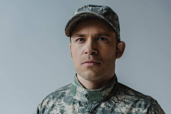 Soldado molesto en uniforme militar llorando durante el día conmemorativo aislado en gris - foto de stock