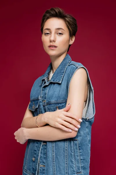 Young model with short hair looking at camera while posing on dark red background — Stock Photo