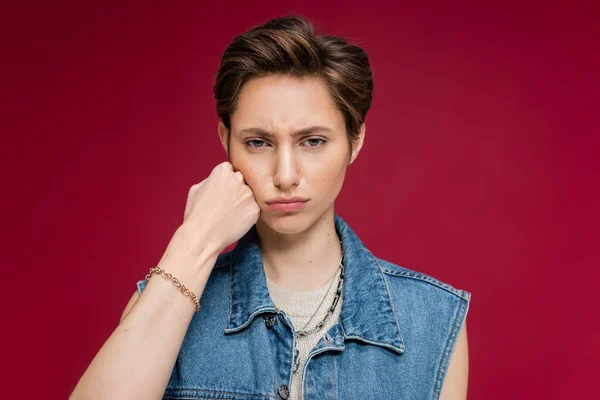 Sad young woman with short hair looking at camera on burgundy background — Stock Photo
