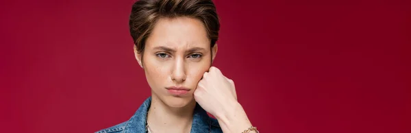 Sad young woman with short hair looking at camera on burgundy background, banner — Stock Photo