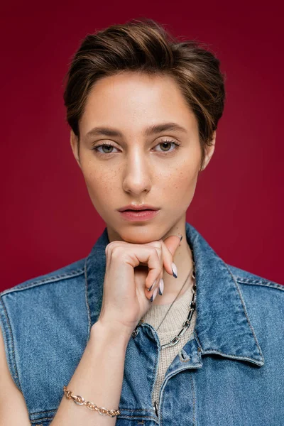 Porträt eines stylischen Models in Jeansweste, das auf weinrotem Hintergrund in die Kamera blickt — Stockfoto