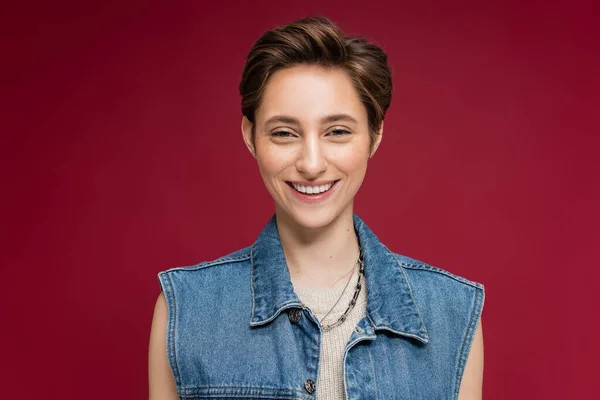 Happy young model in denim vest smiling on burgundy background — Stock Photo