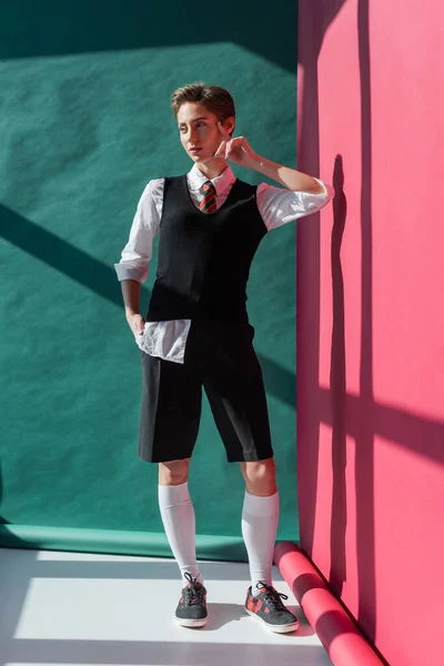 Full length of young woman with short hair posing in school uniform on pink and green — Stock Photo